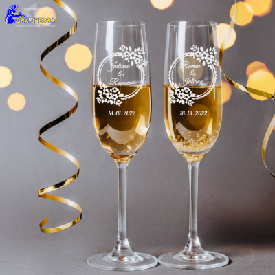 Duas taças de champanhe personalizadas com flores brancas e textos, em fundo cinzento com decorações douradas