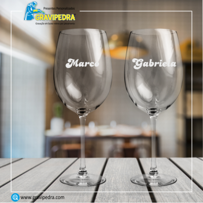 Dois copos de vinho gravados com os nomes Marco e Gabriela numa mesa de madeira