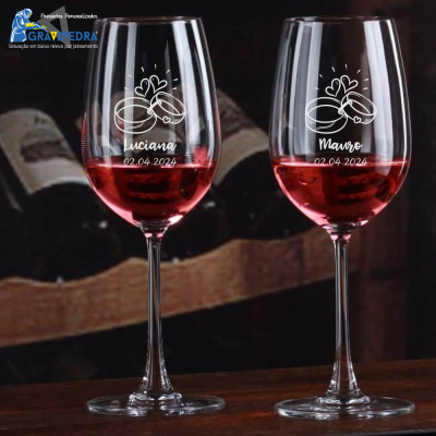 Duas taças de vinho com gravação personalizada e vinho tinto, em ambiente de madeira e caixas de vinho