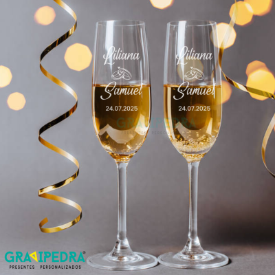 Dois copos de champanhe gravados com nomes e data decorados com fitas douradas.