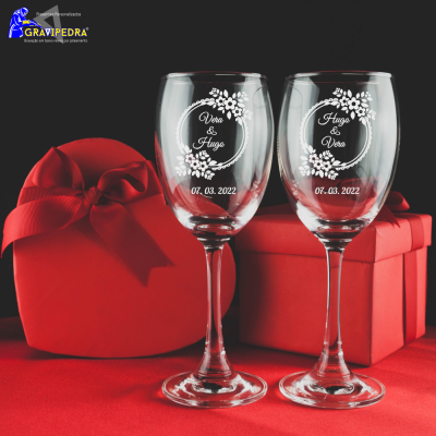 Dois copos de vinho gravados com nomes e data junto a duas caixas de presente vermelhas.