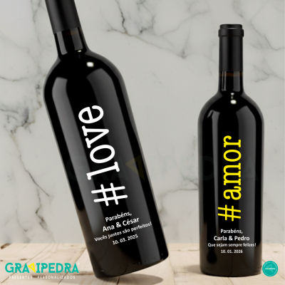 Duas garrafas de vinho preto com rótulos personalizados e texto em português, sobre mesa de madeira e fundo de mármore.