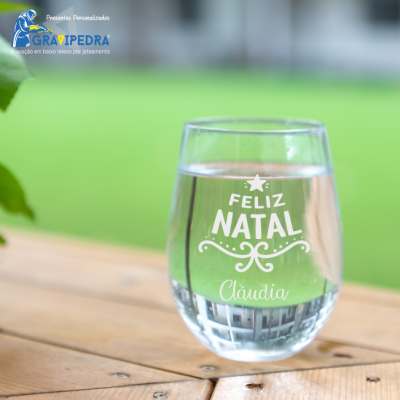 Copo de vidro com gravação Feliz Natal Cláudia sobre mesa de madeira