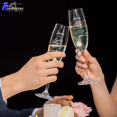 Taças de champanhe gravadas com nomes e datas em fundo escuro com vela e flores