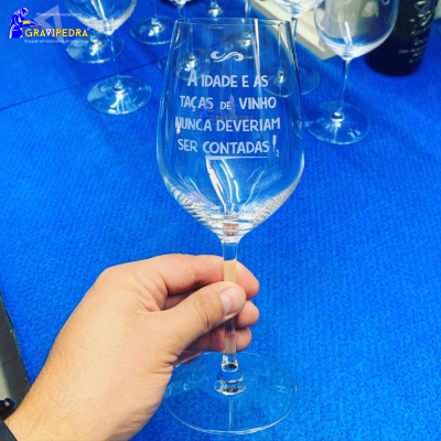 Copo de vinho de vidro com texto gravado sobre mesa azul, rodeado por mais copos similares