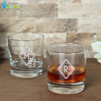 Dois copos de vidro gravados com letras M e R sobre superfície castanha e fundo de pedra clara