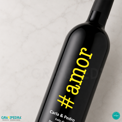 Garrafa de vinho preta com texto amarelo #amor e texto branco com nomes Carla & Pedro sobre fundo marmoreado