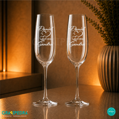 Duas taças de champanhe gravadas com nomes e data, em cenário decorativo com iluminação quente.
