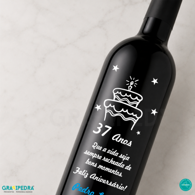 Garrafa de vinho preta com decoração de bolo e texto de aniversário em branco.