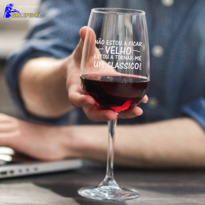 Taça de vinho tinto com texto impresso em branco, mãos segurando a taça, pessoa de camisa azul ao fundo