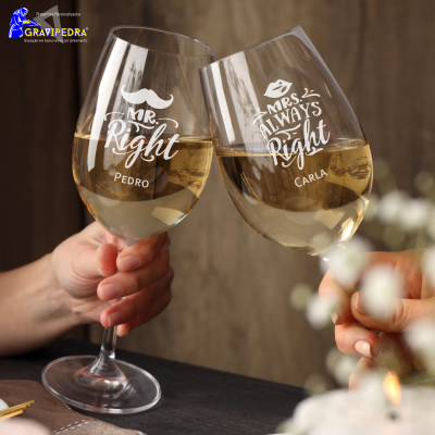 Dois copos de vinho com texto personalizado a brindar sobre uma mesa e fundo de madeira.