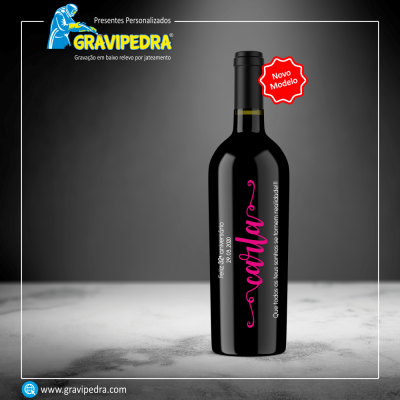Garrafa de vinho preta com rótulo de texto em rosa e branco em fundo cinzento, marca GRAVIPEDRA ao fundo