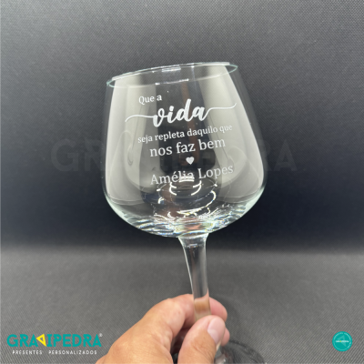 Taça de vinho transparente com gravação personalizada em branco numa mão sobre fundo preto.