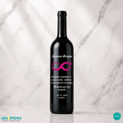 Garrafa de vinho preta com rótulo personalizado branco e rosa, texto em português, sobre fundo mármore branco.