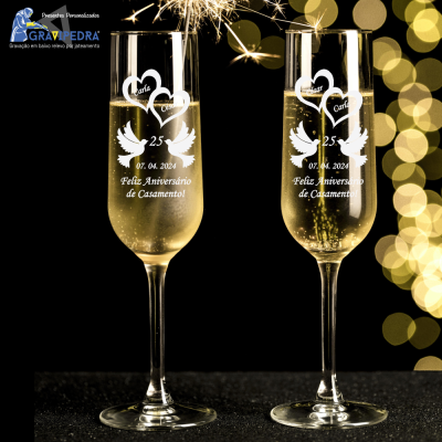 Taças de champanhe gravadas para 25º aniversário de casamento com nomes e data, bebida dentro, fundo preto com luzes amarelas