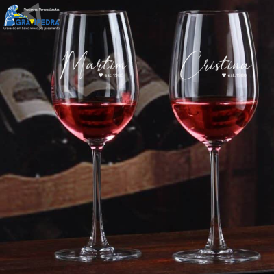 Dois copos de vinho tinto personalizados com nomes em vidro sobre mesa de madeira