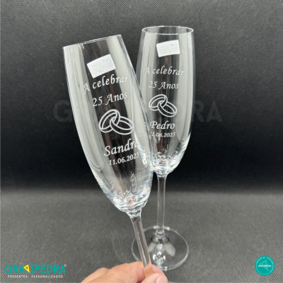 Dois copos de champanhe transparentes com gravações personalizadas em branco para celebração de 25 anos, com nomes e data.
