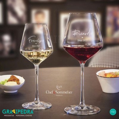 Duas taças de vinho personalizadas com nomes e datas, vinho branco e tinto, sobre mesa com petiscos