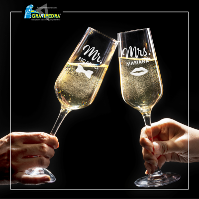 Dois copos de champanhe personalizados com texto e desenhos, um masculino e outro feminino, em fundo preto.