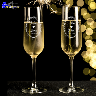 Duas taças de champanhe gravadas com nomes e data, fundo preto com luzes douradas e fogo-de-artifício.