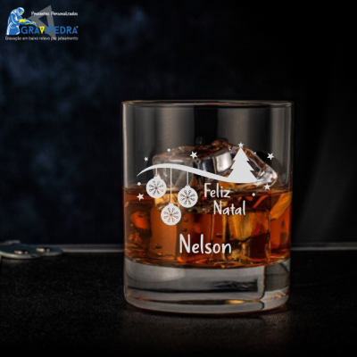 Copo de vidro com bebida castanha, gelo e gravação branca temática de Natal
