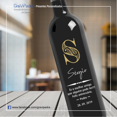 Garrafa preta gravada personalizada com texto e inicial 'S' numa mesa de madeira
