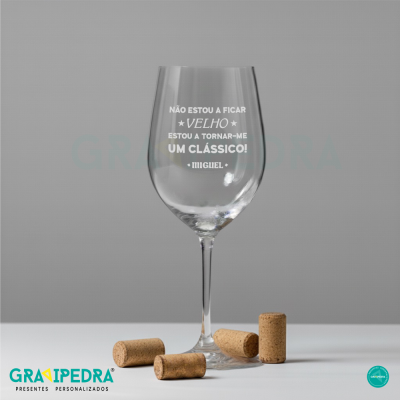 Copo de vinho transparente com texto gravado e rolhas de cortiça.