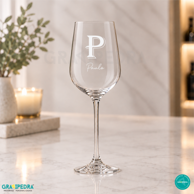 Cálice de vinho transparente com gravação P Paulo sobre mesa de mármore