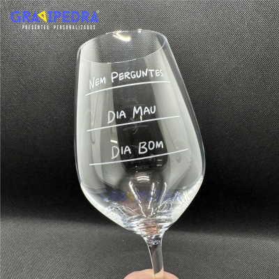 Copo de vinho transparente com texto gravado em branco e fundo preto.