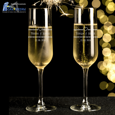 Duas taças de champanhe gravadas com nomes e data, fundo com luzes douradas desfocadas