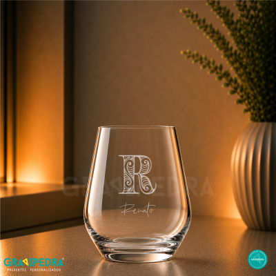 Copo de vidro gravado com letra R e nome Renato, em ambiente com iluminação quente e vaso com plantas.
