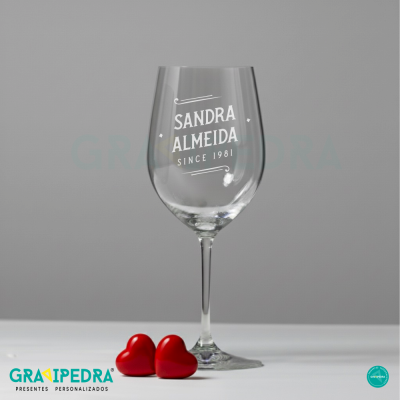 Copo de vinho de vidro com texto personalizado e corações vermelhos ao lado.