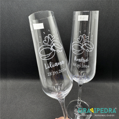 Duas taças de champanhe gravadas com nomes, data e desenhos de alianças sobre fundo preto