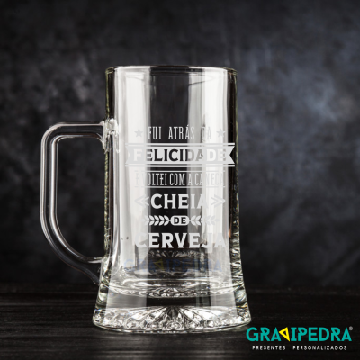 Caneca de vidro transparente com texto branco 'FUI ATRÁS DA FELICIDADE VOLTEI COM A CANECA CHEIA DE CERVEJA'