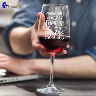 Taça de vinho tinto com texto gravado, mão segurando e fundo com pessoa e laptop.