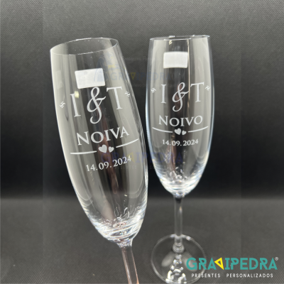 Dois copos de champagne transparentes com gravação personalizada em branco e fundo preto.