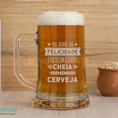 Caneca de cerveja transparente com texto impresso, cheia de cerveja, sobre mesa clara.