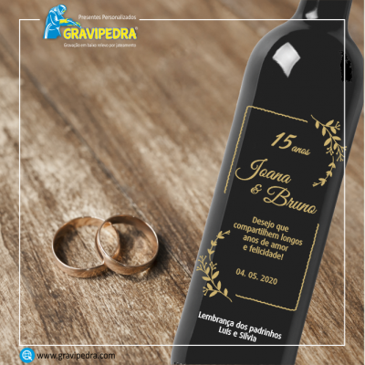 Garrafa preta personalizada para celebração de 15 anos com texto dourado e dois anéis dourados sobre mesa de madeira