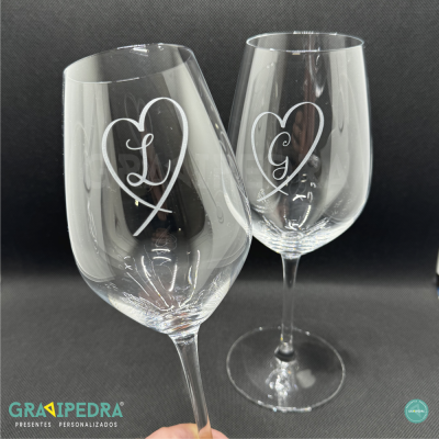 Dois copos de vinho transparentes com corações e letras L e G gravados.