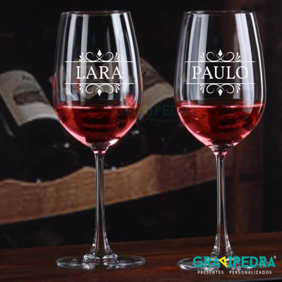 Dois copos de vinho tinto personalizados com nomes LARA e PAULO em ambiente de adega