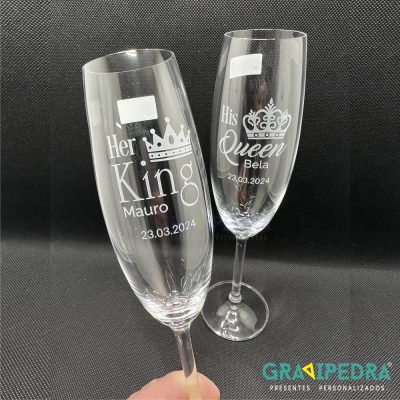 Dois copos de champanhe personalizados com gravações em branco, um 'Her King Mauro 23.03.2024' e outro 'His Queen Bela 23.03.2024'.
