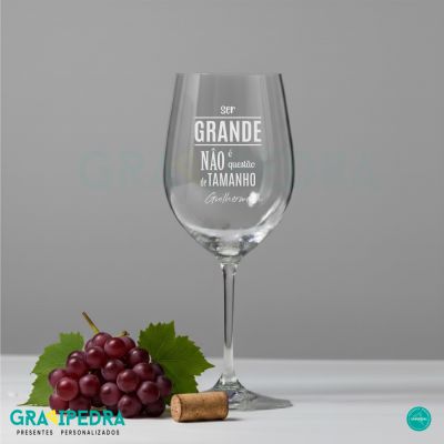 Copo de vinho transparente com mensagem em branco, uvas roxas e rolha sobre superfície branca