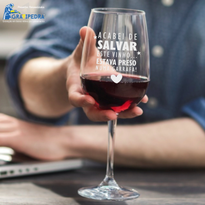 Copo de vinho com texto impresso, vinho tinto e mão segurando sobre mesa