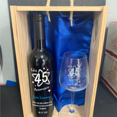 Garrafa de vinho e taça com texto de aniversário numa caixa de madeira com forro azul