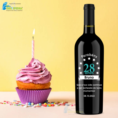 Garrafa de vinho personalizada com texto comemorativo ao lado de cupcake rosa com vela acesa