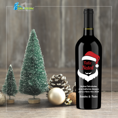 Garrafa de vinho preta com rótulo de Natal personalizada junto a árvores e pinhas decorativas