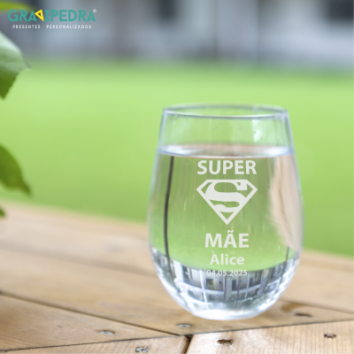 Copo de vidro com gravação branca 'SUPER MÃE Alice 04.05.2025' numa mesa de madeira.