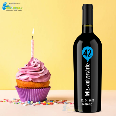 Garrafa de vinho preta com rótulo azul e branco ao lado de cupcake com vela