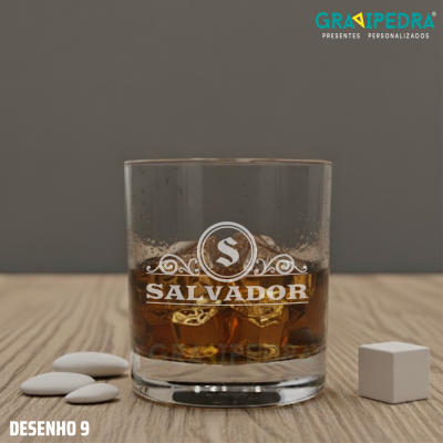 Copo de vidro com bebida e gravação personalizada 'SALVADOR' sobre mesa de madeira