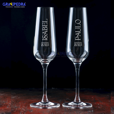 Dois copos de champanhe personalizados em vidro, com gravação de nomes e ano, sobre fundo preto
